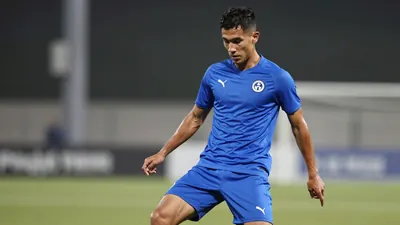 A 25-year-old right-back with a lean athletic build, wearing a solid blue training jersey, stands on a football pitch...