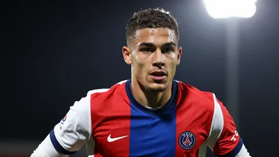 A photorealistic image of a 21-year-old Belgian player in a red and blue jersey with white sleeves, playing for Paris FC...