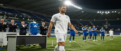 Pablo Pagis, 23, in a plain Paris FC home kit of navy blue shirt and white shorts, standing on a sunlit pitch with a...