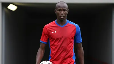 A 20-year-old, tall, Franco-Ivorian striker with a shaved head, wearing a red and blue jersey with a smooth, unbroken...