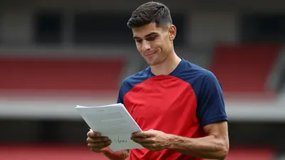 Mid-30s athletic forward, dark hair, focused eyes, waist-up, wearing a plain blue and red training shirt (solid navy...