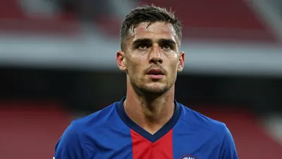 Mid-30s athletic midfielder, lean build, intense gaze, head-and-shoulders shot, wearing a plain blue shirt with a red...
