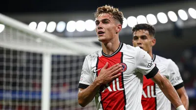 A tight action crop of a young German player, Paris Brunner, celebrating his goal with a teammate, both wearing red and...