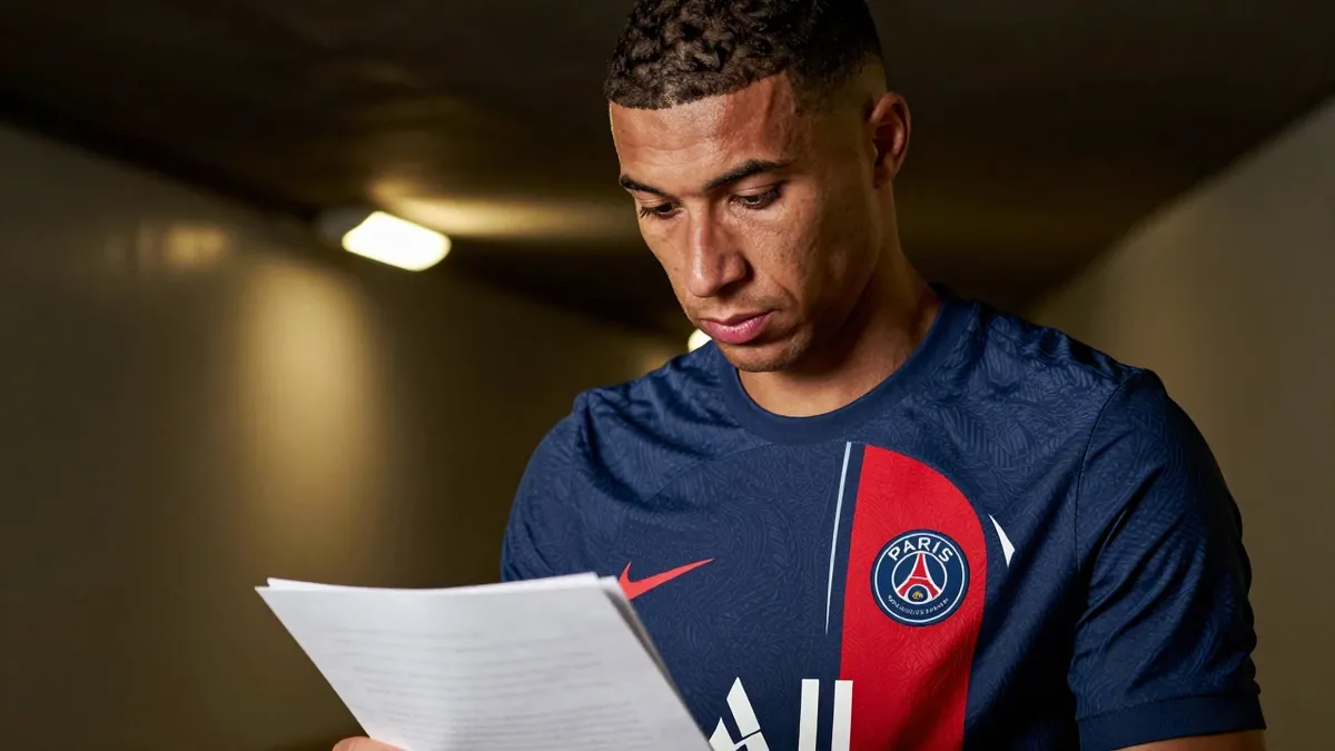 A close-up shot of a focused, 30-year-old Paris FC midfielder, dressed in a plain, unmarked blue and red home kit made of...